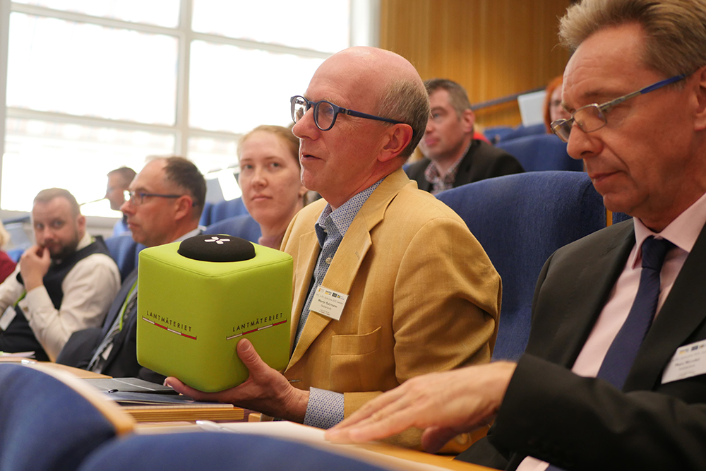  A man with blue glasses and a yellow jacket holds a pea green cube.