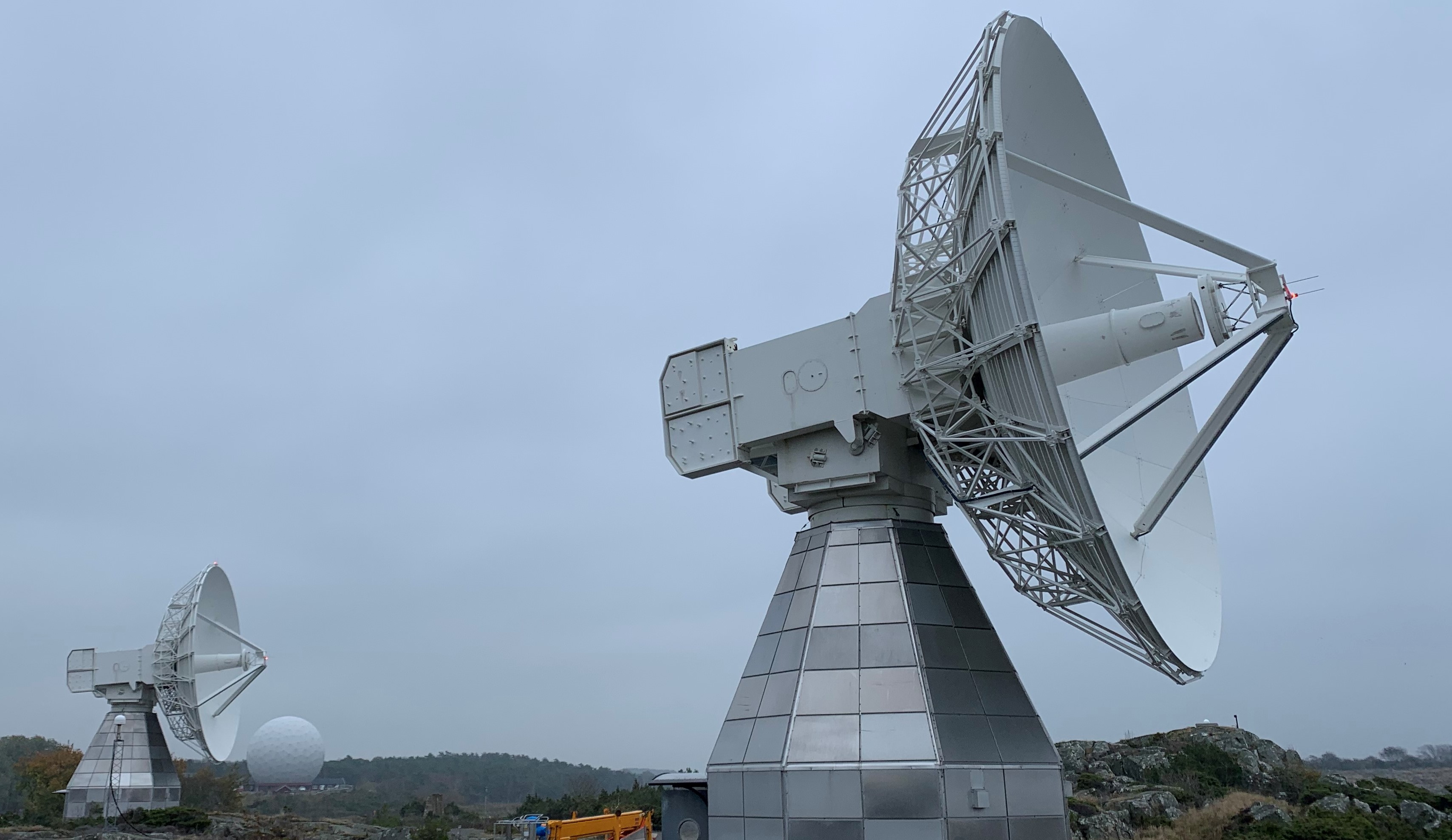 Foto av ett av radioteleskopen på Onsala. I bakgrunden syns ett annat radioteleskop, samt skyddet till ett av teleskopen. Teleskopskyddet ser ut som en jättestor golfboll.