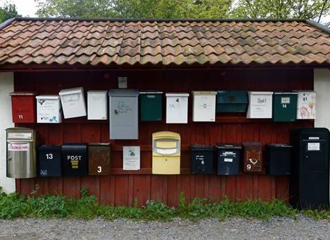 A dozen mailboxes in a row in front of a red-painted older wooden house